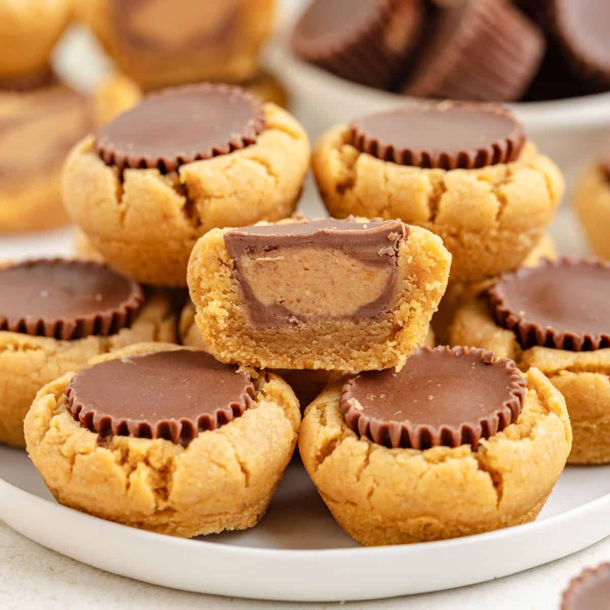 Peanut butter cup cookies with chocolate centers on a plate; one is halved, revealing the filling.