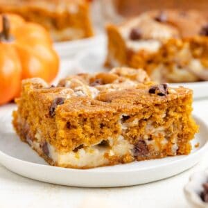 Close-up of a pumpkin earthquake cake on a white plate, with another slice and pumpkin behind.