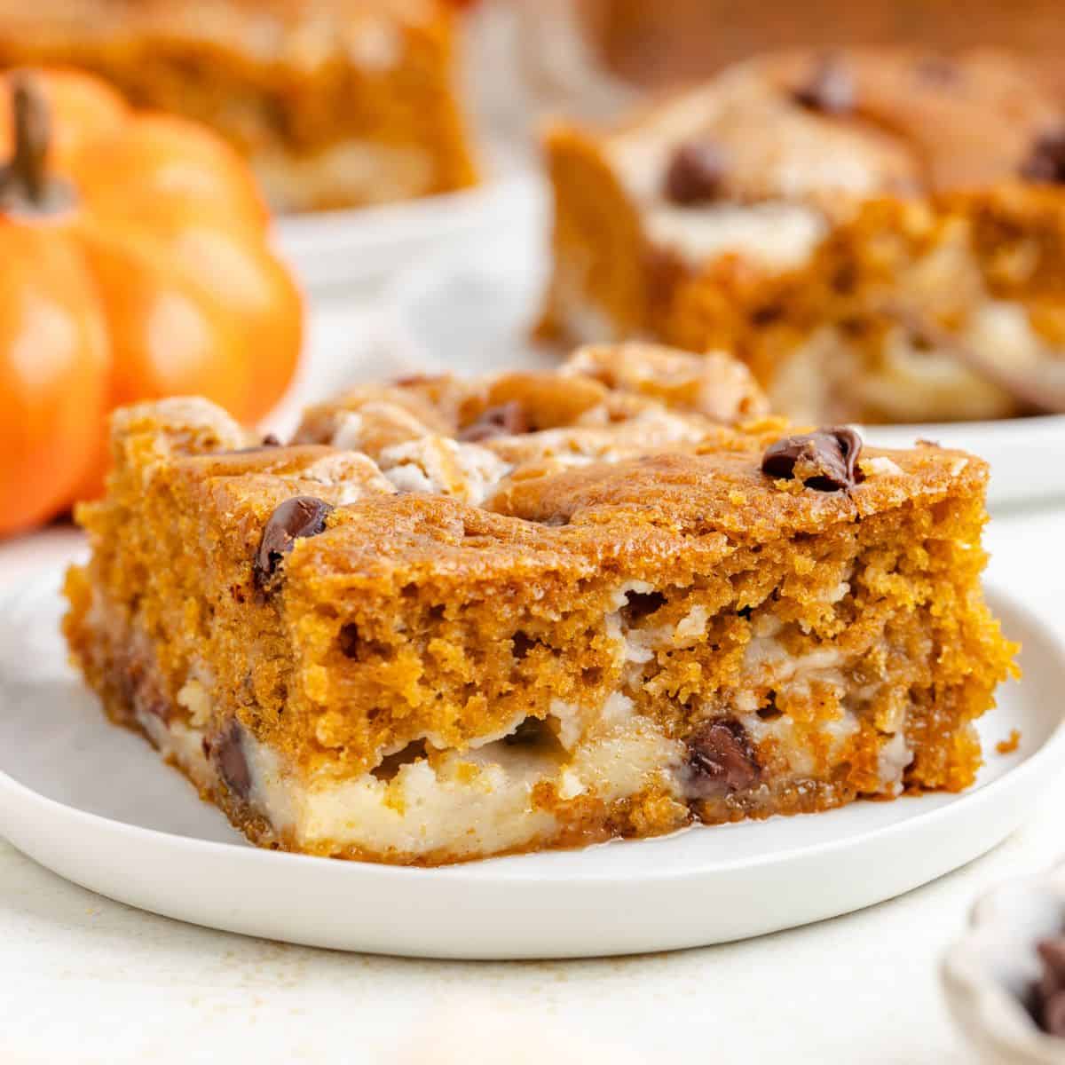 Close-up of a pumpkin earthquake cake on a white plate, with another slice and pumpkin behind.