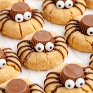 Peanut butter spider cookies with chocolate peanut butter cups, candy eyes, and chocolate legs on a light background.