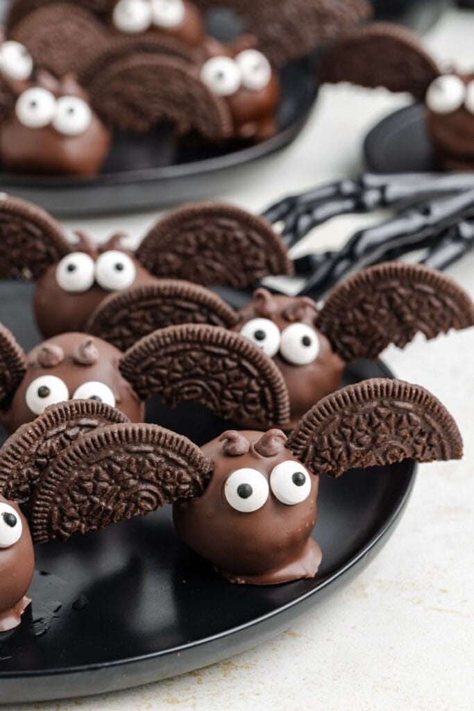 Chocolate bat truffles  with candy eyes and Oreo wings, displayed on a black plate.