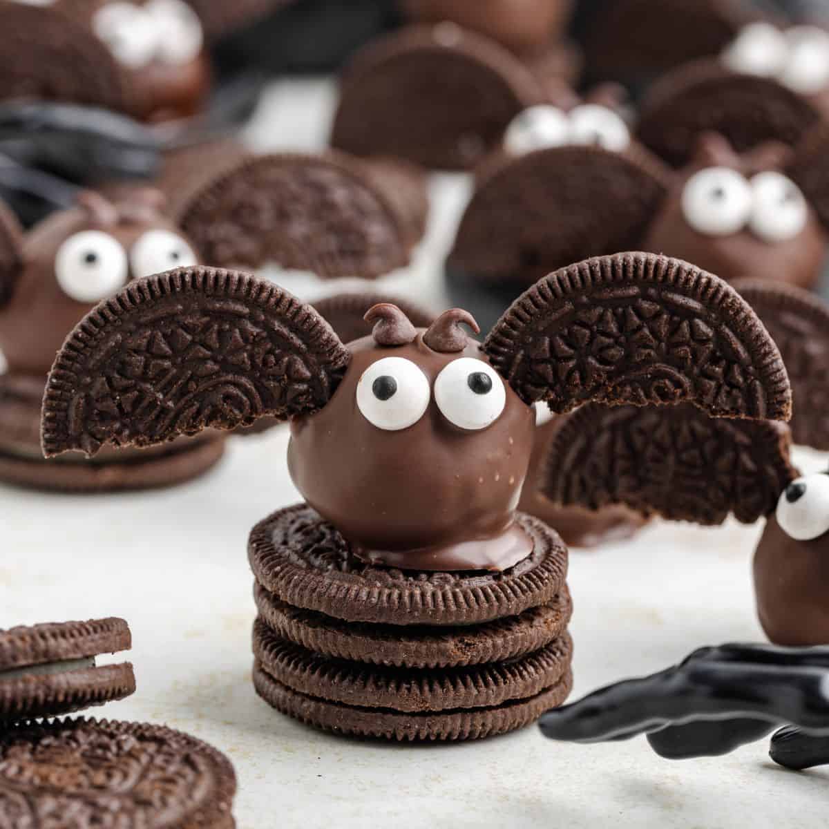 Bat-shaped chocolate cookies with candy eyes and cookie wings rest on stacked chocolate sandwich cookies.