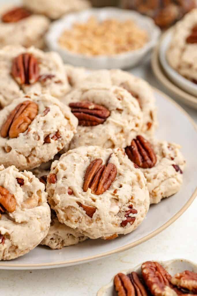 Plate of butter pecan cake mix cookies topped with pecan halves, with extra cookies and nuts visible in the background.
