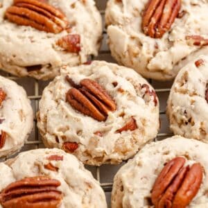 Freshly baked butter pecan cookies topped with pecans, cooling on a wire rack in a close-up view.