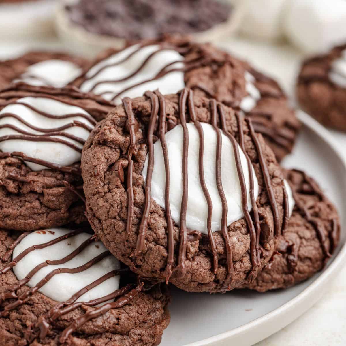 Plate of hot chocolate cookies with melted marshmallow centers and a drizzle of chocolate on top.