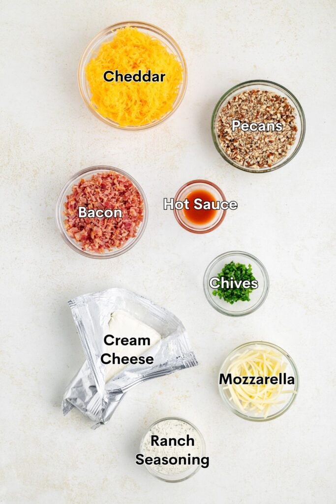 Cheese ball ingredients—cheddar, pecans, bacon, hot sauce, chives, cream cheese, mozzarella—arranged on a counter.