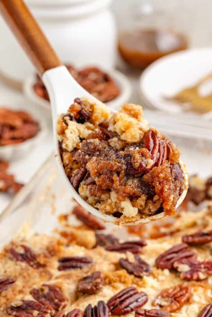 Spoon lifts pecan pie dessert with crumbly topping above a baking dish filled with more of the same dessert.