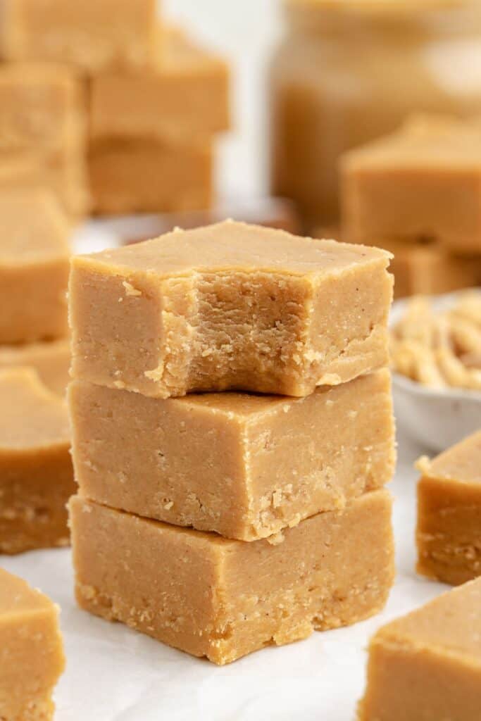 Stacked peanut butter fudge, one piece bitten, with more fudge and a jar blurred in the background.