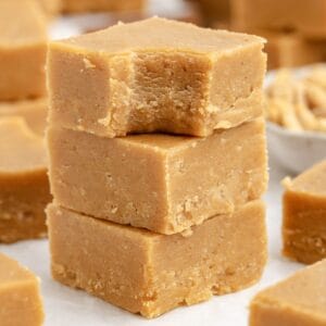 Stack of 2 ingredient peanut butter fudge pieces, top piece bitten, with more fudge blurred in the background.