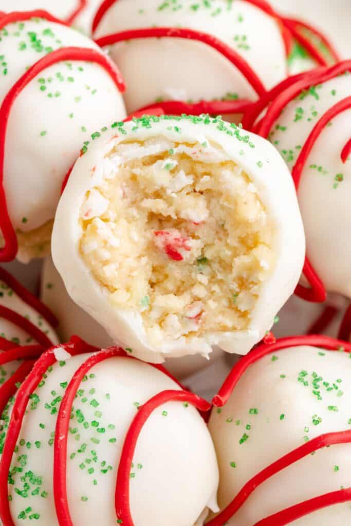 Christmas tree cake balls with green sprinkles and red icing; one is bitten, revealing sprinkles inside.