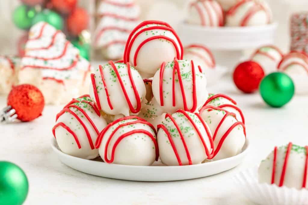Plate of Little Debbie Christmas Tree Cake balls truffles with red icing and green sprinkles, surrounded by festive holiday treats.