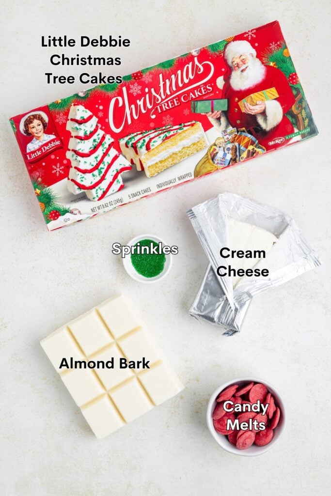 Little Debbie Christmas Tree Cakes, sprinkles, cream cheese, almond bark, and red candy melts on a white surface.
