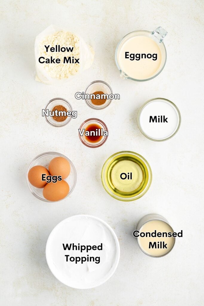 Top-down view of labeled dessert ingredients: yellow cake mix, eggnog, milk, oil, eggs, spices, vanilla.