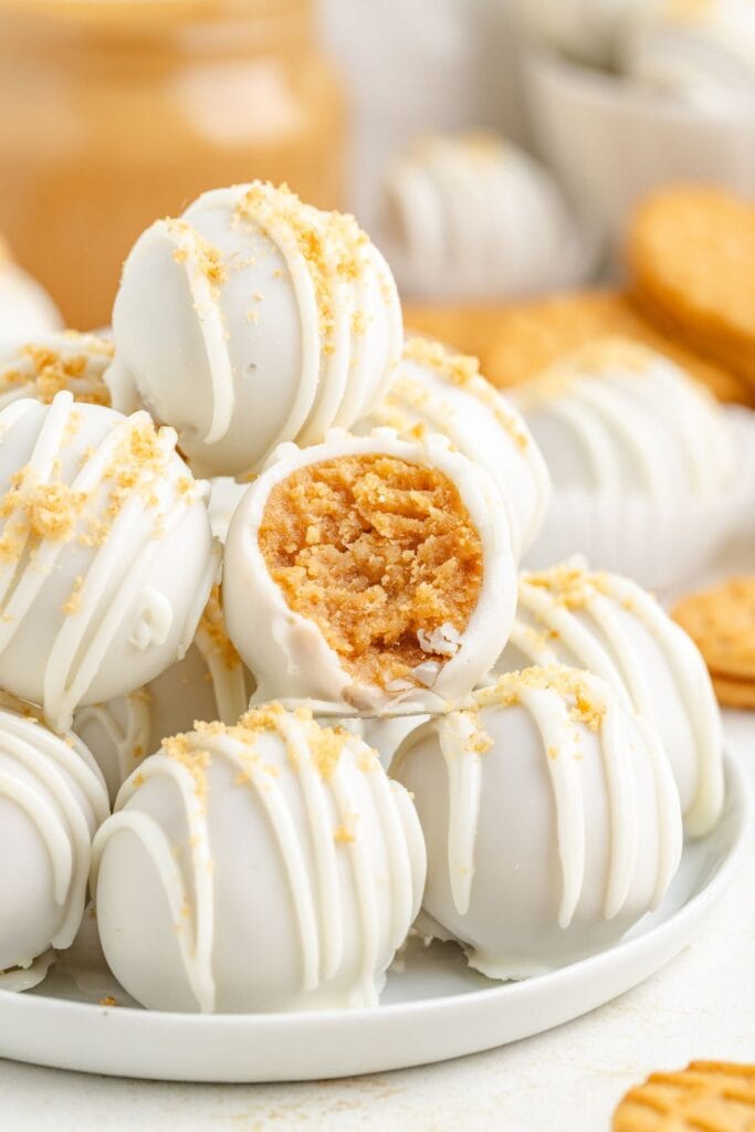 White chocolate-coated Nutter Butter truffles on a plate, some crumb-topped, one bitten to show creamy filling inside.