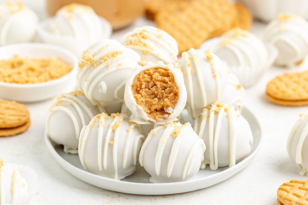 Plate of Nutter Butter Balls, some with cookie crumbs, one bitten to reveal peanut butter filling.
