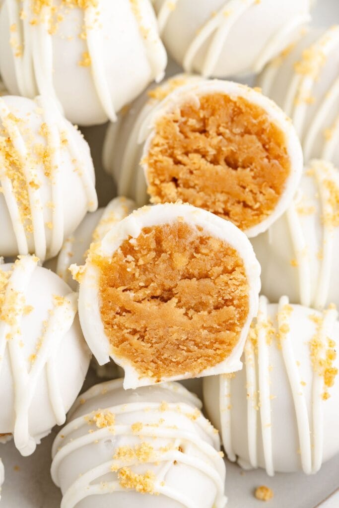 Close-up of peanut butter balls with crumb topping; one is cut open showing the light brown, crumbly filling inside.
