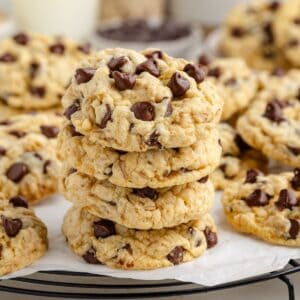 A stack of oatmeal chocolate chip cookies on a wire rack, with more cookies on parchment nearby.