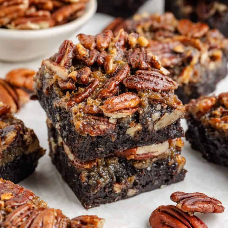 Two stacked pecan pie brownies surrounded by more brownies and scattered pecans.