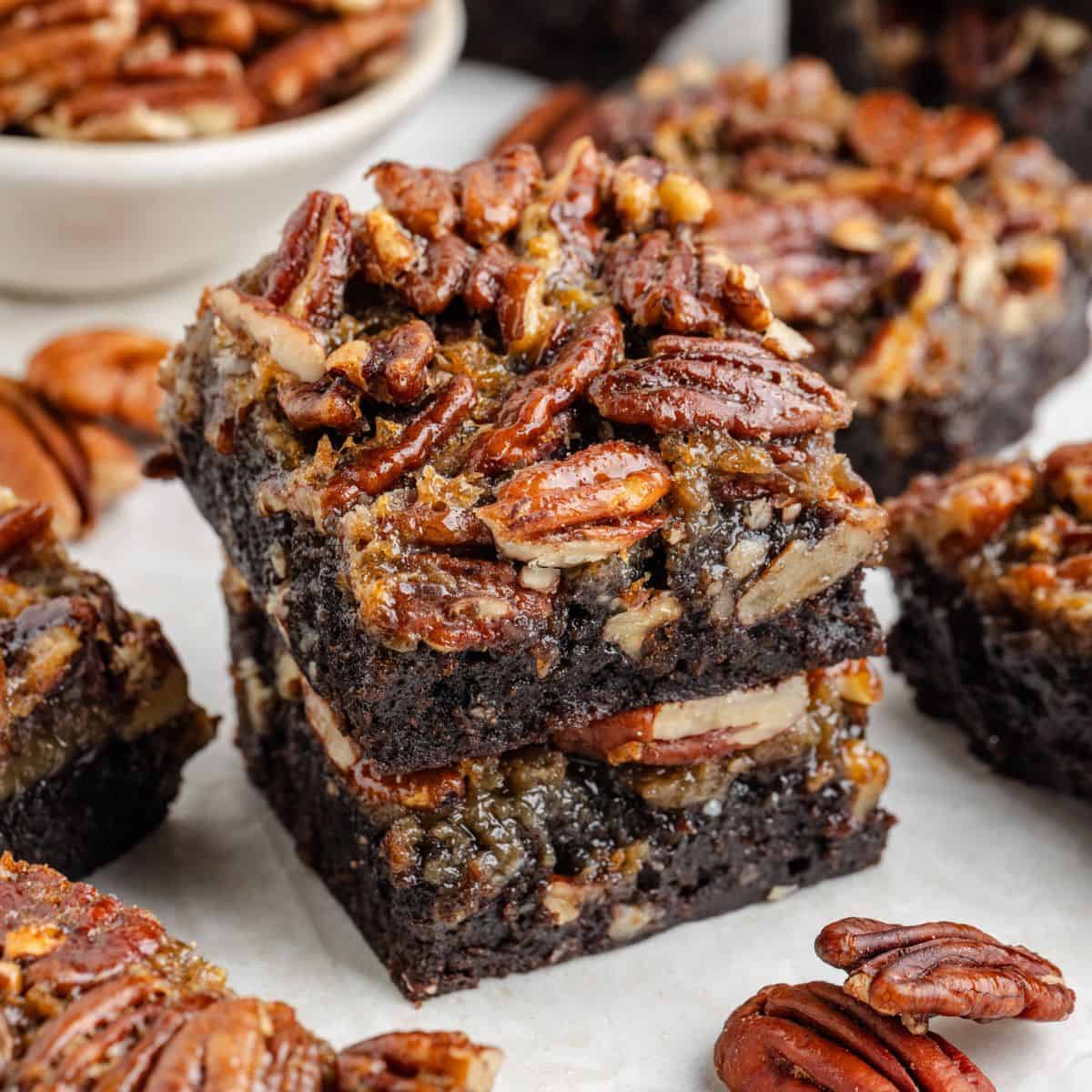 Two stacked pecan pie brownies surrounded by more brownies and scattered pecans.