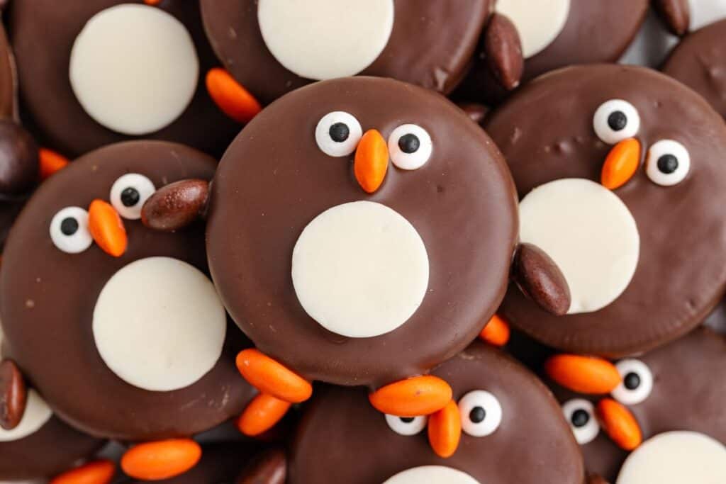 Penguin Oreos with white chocolate bellies, candy eyes, and orange and brown candy details.