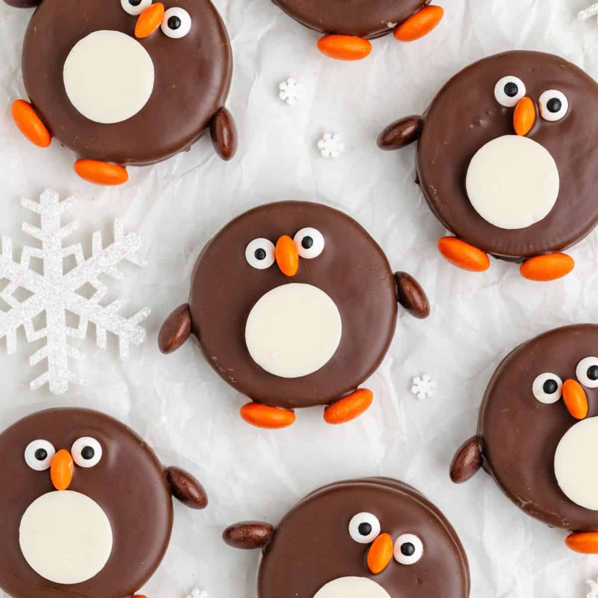 Penguin Oreos with candy details on a white surface, snowflake decoration visible nearby.