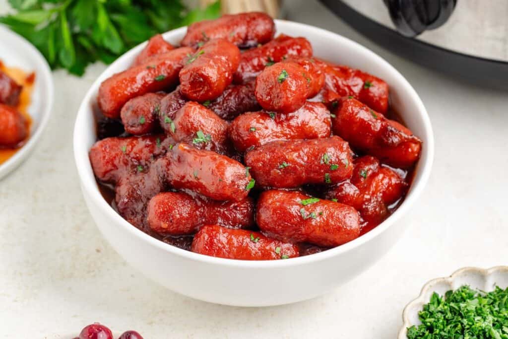 Slow Cooker cranberry little smokies, garnished with parsley, served in a white bowl.