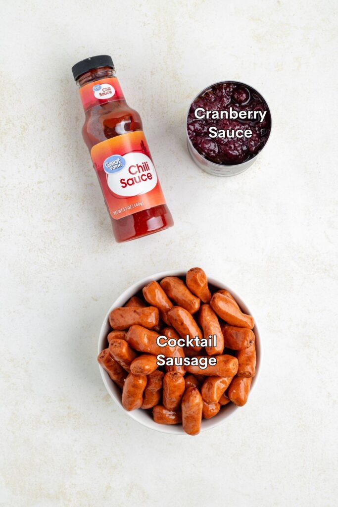 Chili sauce, cranberry sauce can, and bowl of cocktail sausages on a light-colored surface.