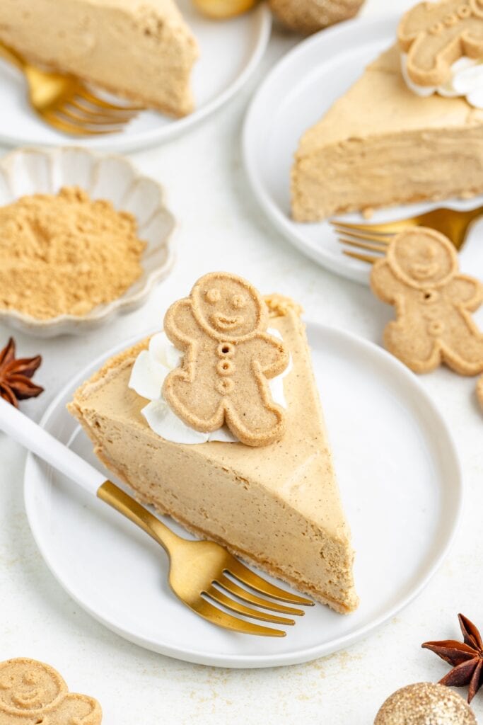 A slice of gingerbread pie with whipped cream and a gingerbread cookie on a white plate with a gold fork.