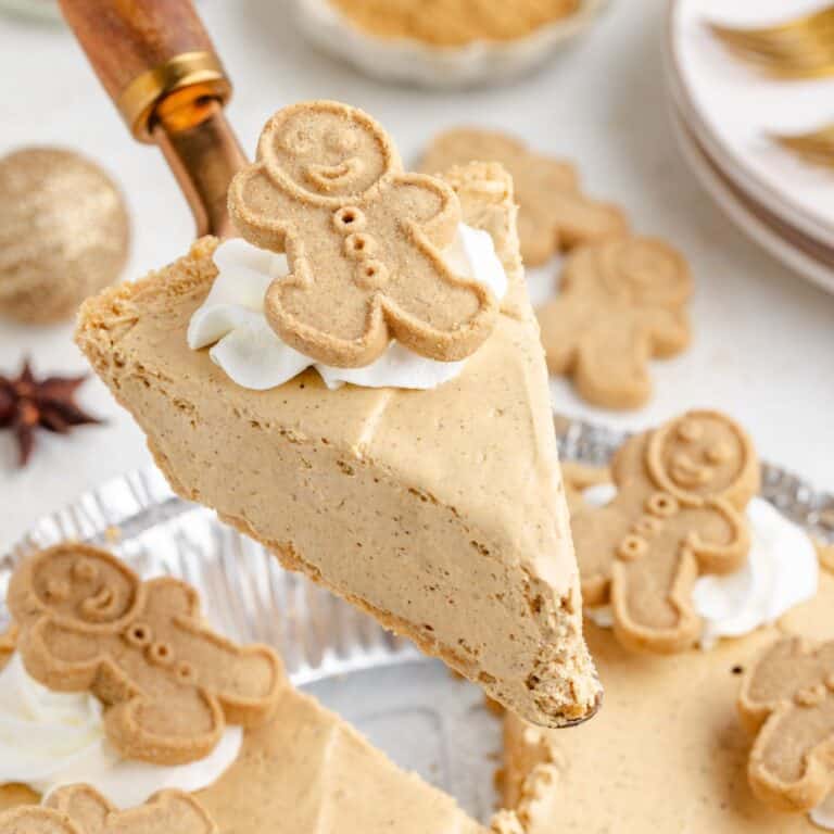 A slice of creamy no bake gingerbread pie with whipped cream and a gingerbread cookie, lifted from a tin of decorated slices.