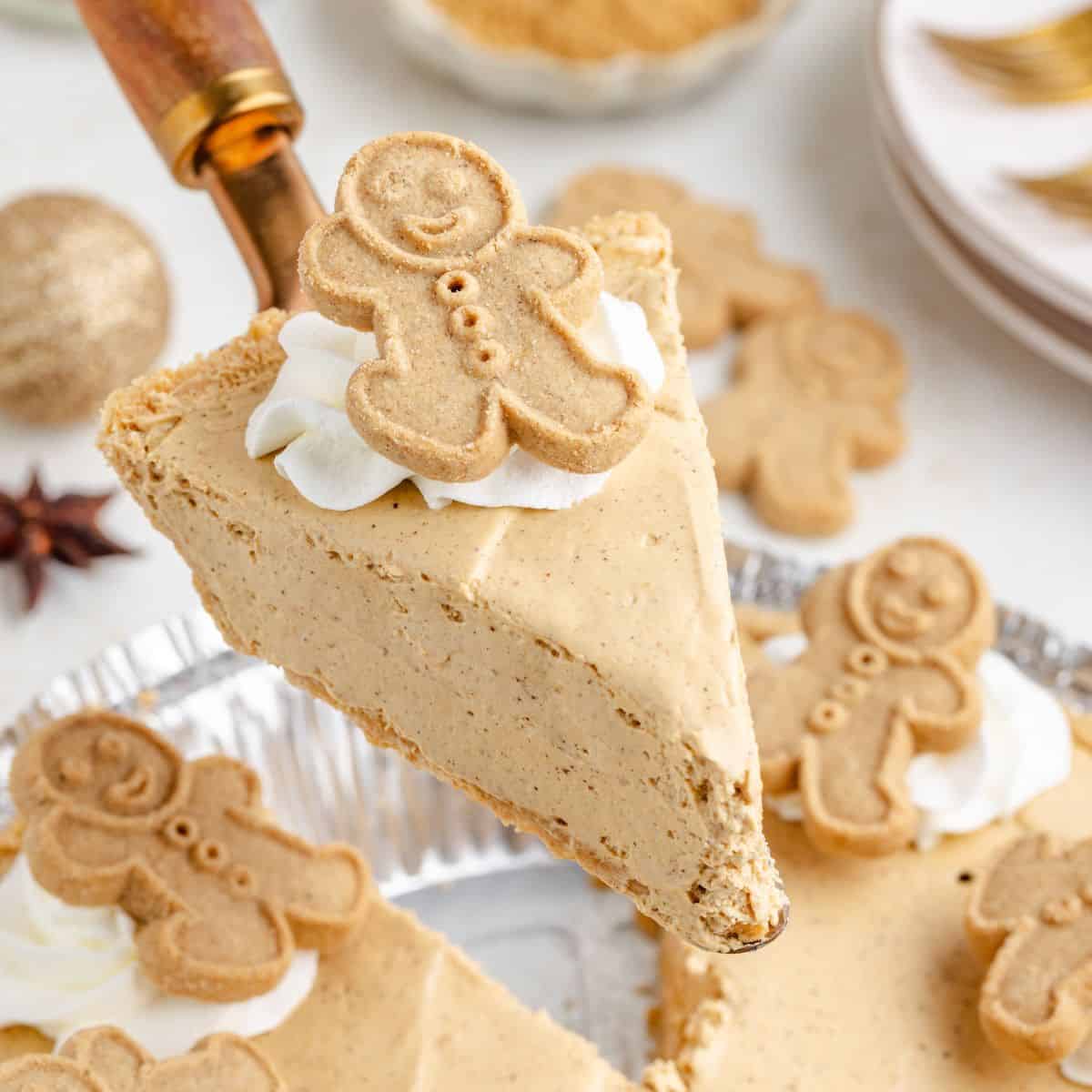 A slice of creamy no bake gingerbread pie with whipped cream and a gingerbread cookie, lifted from a tin of decorated slices.