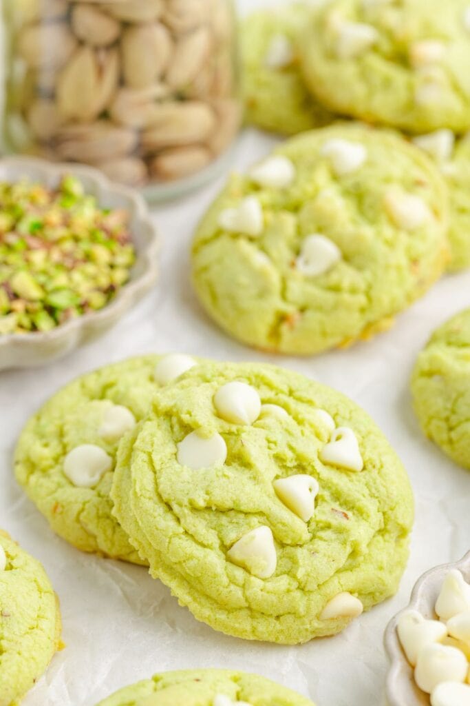 Pistachio pudding cake mix cookies on parchment, pistachios and a jar in the background.