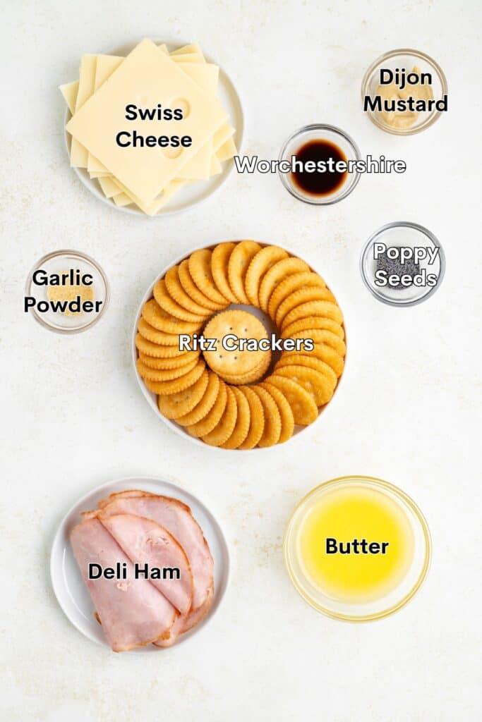 Swiss cheese, ham, crackers, butter, seasonings and condiments arranged in bowls and plates on a white surface.