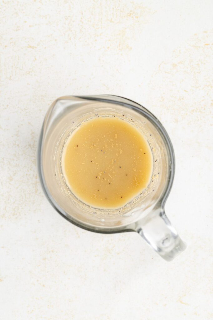Measuring cup with a little light brown liquid and black specks, seen from above on a white surface.