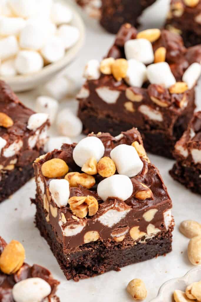 Rocky Road Brownies topped with chocolate fudge, peanuts, and mini marshmallows on a white surface.