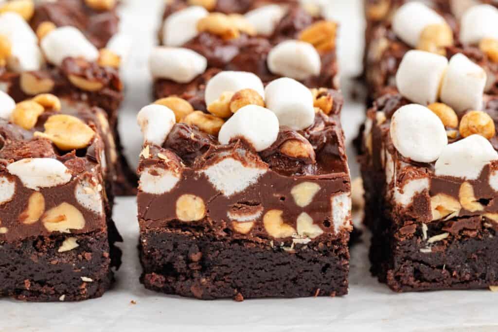 Close-up of easy rocky road brownies topped with nuts, marshmallows, and chocolate chunks, arranged in neat rows on parchment.