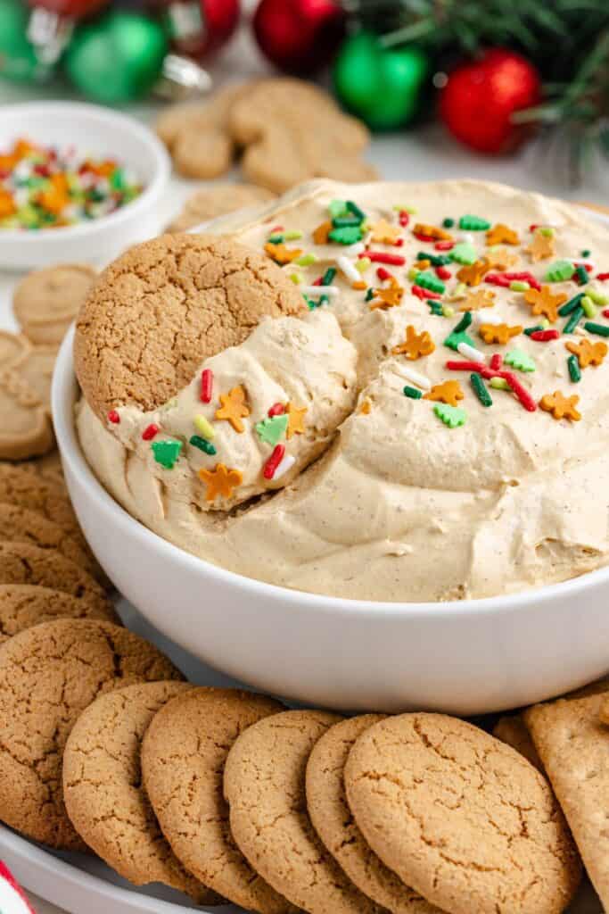 Creamy dip with holiday sprinkles in a white bowl, surrounded by gingersnap cookies and festive ornaments.