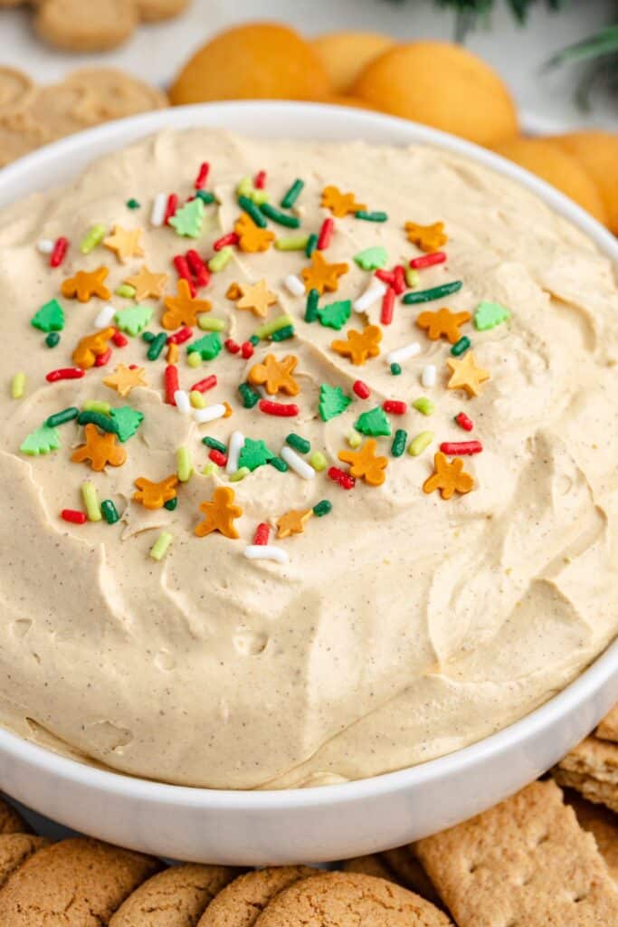 Bowl of gingerbread dip with Christmas sprinkles, surrounded by assorted cookies.