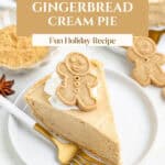 Slice of gingerbread cream pie with whipped cream and a gingerbread cookie on a white plate, gold fork beside.