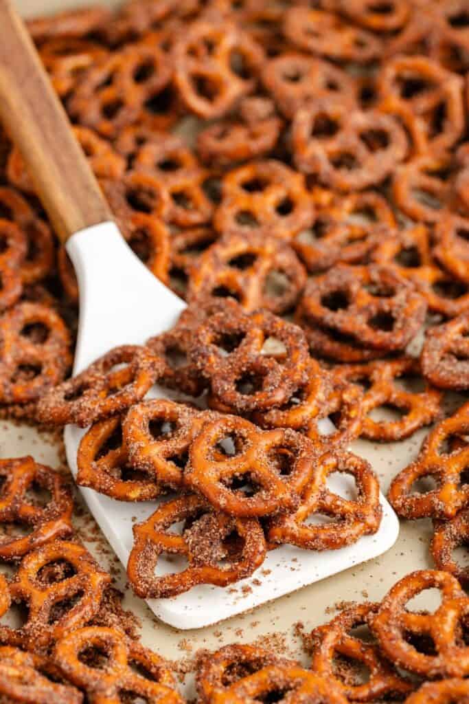 A white spatula lifts cinnamon sugar mini pretzels from a baking sheet full of more coated pretzels.