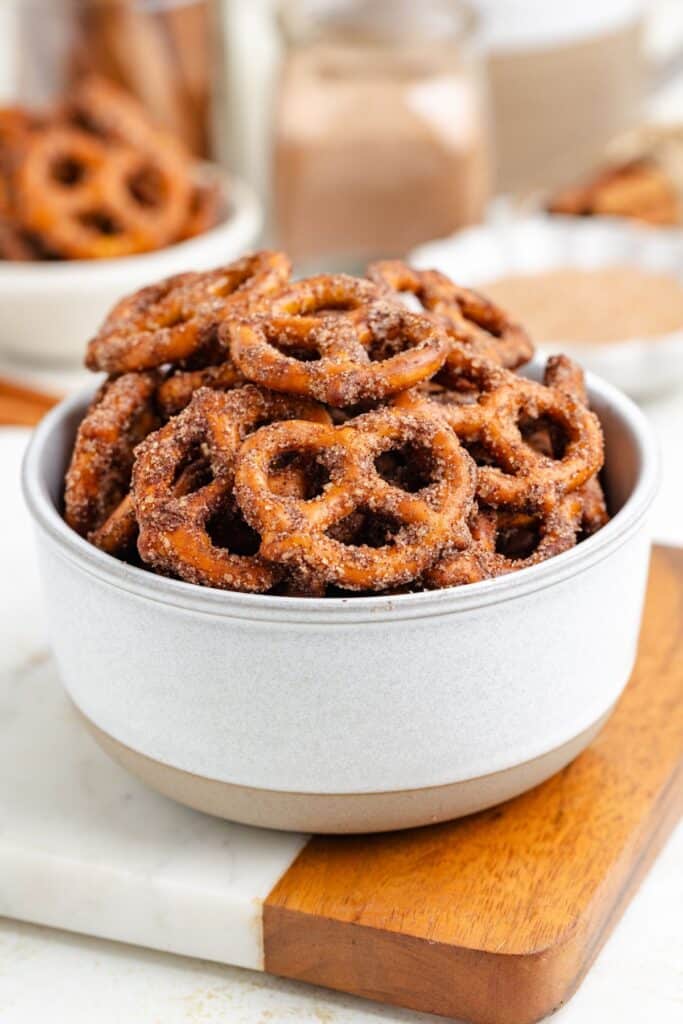 A white bowl of cinnamon sugar pretzels on a marble and wood surface.