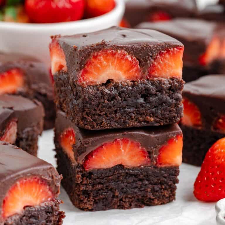Two stacked chocolate covered strawberry brownies, more brownies and strawberries in the background.