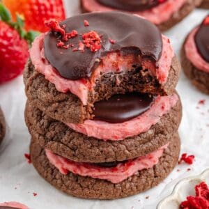 Stacked chocolate strawberry cookies topped with strawberry frosting and chocolate ganache.
