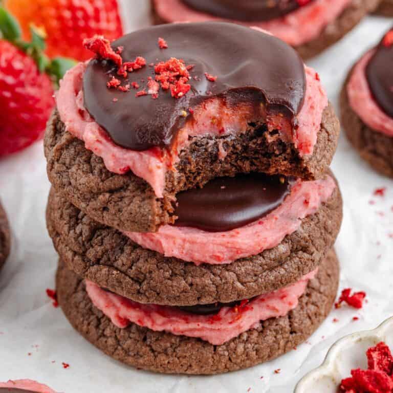 Stacked chocolate strawberry cookies topped with strawberry frosting and chocolate ganache.