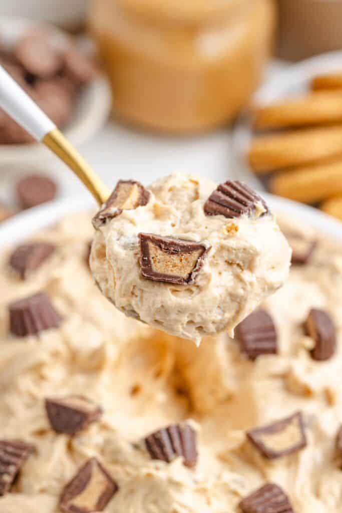 Spoonful of Peanut Butter Marshmallow Fluff topped with chopped peanut butter cups; more dessert and candy pieces in background.