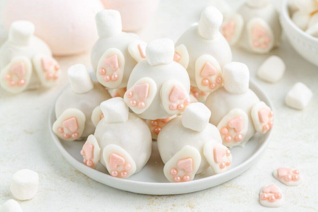 Plate of Bunny Butt Truffles with marshmallow tails and fondant feet; extra marshmallows and fondant scattered nearby.