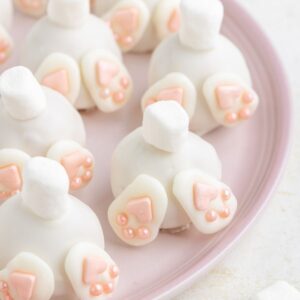 Bunny butt truffles with white coating, marshmallow tails, and pink feet on a light pink plate.