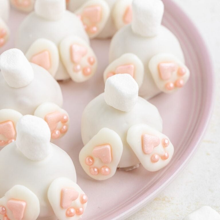 Bunny butt truffles with white coating, marshmallow tails, and pink feet on a light pink plate.