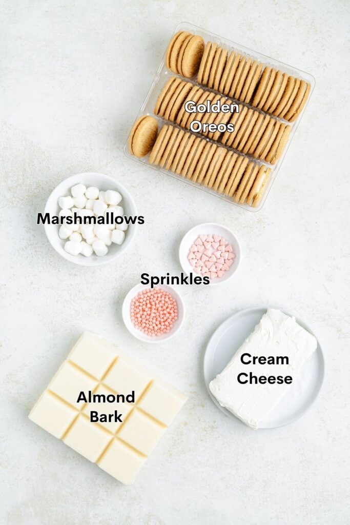 Golden Oreos, marshmallows, pink sprinkles, cream cheese, and almond bark arranged on a light surface.
