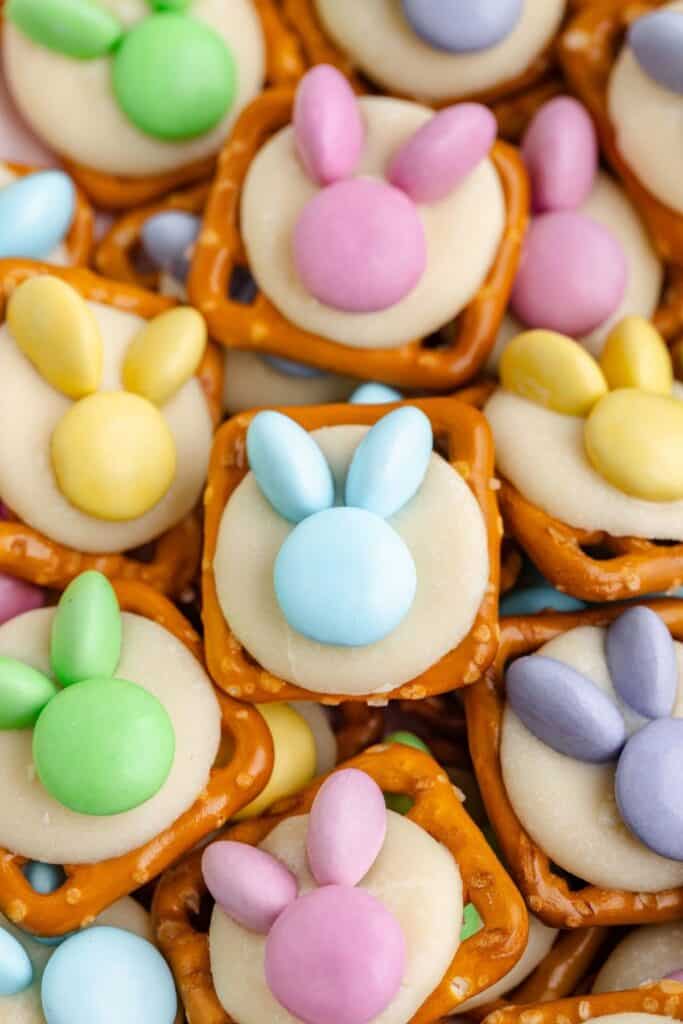 Pretzel bunny treats with white chocolate and pastel candies arranged as bunny faces, shown in a close-up view.
