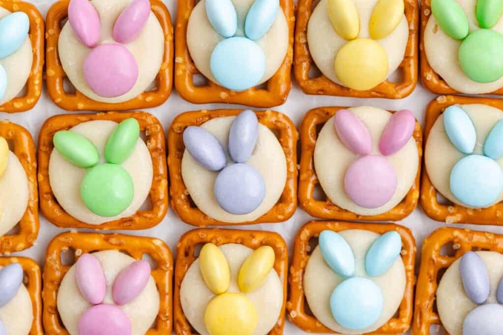 Square bunny pretzels with white candy and pastel chocolates arranged as bunny faces in neat rows.